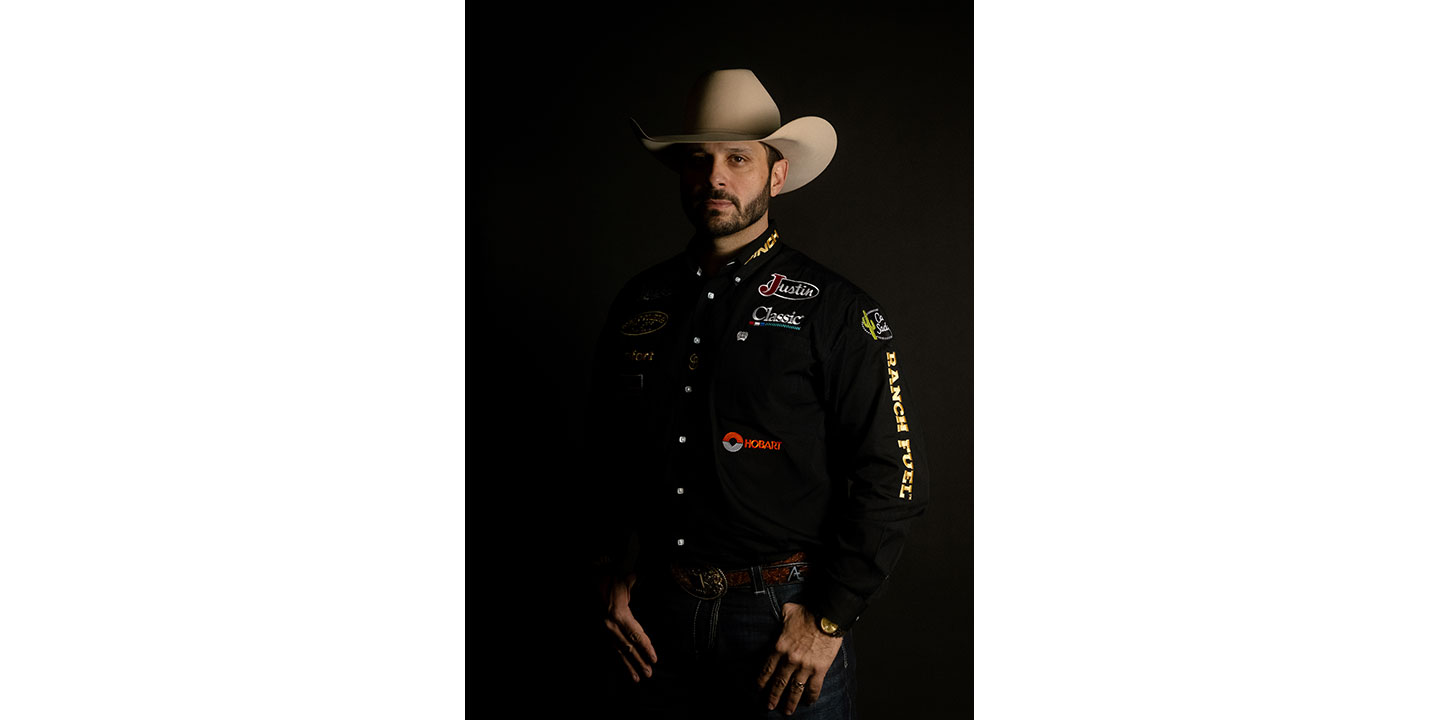 Anthony Lucia vistiendo una camisa negra y un sombrero de vaquero, mirando a la cámara con su rostro en sombras.